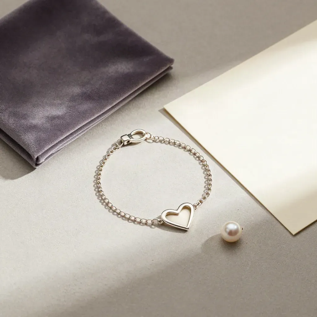 Bracciale a cuore inciso, sacchetto in velluto salvia, perla e cartoncino su cemento chiaro.